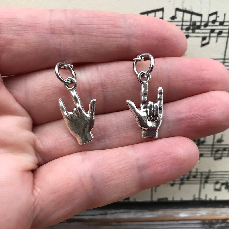 May include: Two silver charm pendants in the shape of a hand making the 'I love you' sign language gesture.