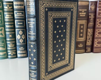Puede incluir: Una colección de libros clásicos, con una edición encuadernada en cuero azul marino de "Padres e hijos" de Iván Turguénev. El libro presenta detalles decorativos dorados y forma parte de la colección The Franklin Library.