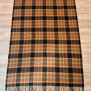 May include: A rectangular plaid blanket in shades of black, gold, and red. The blanket has a fringed edge and a classic tartan pattern. The blanket is made of a soft material, perfect for a cozy evening.