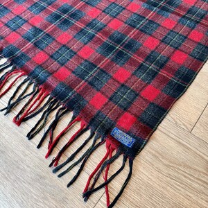 Puede incluir: Bufanda a cuadros rojos, negros y verdes con flecos. La bufanda tiene un patr&oacute;n de cuadros cl&aacute;sico y una etiqueta que dice "Pendleton". Los flecos son una mezcla de rojo, negro y verde.