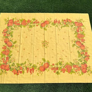 May include: A rectangular yellow tablecloth with a fruit design. The border features a repeating pattern of red berries, green leaves, and orange fruits. The center has a small cluster of the same fruit design.