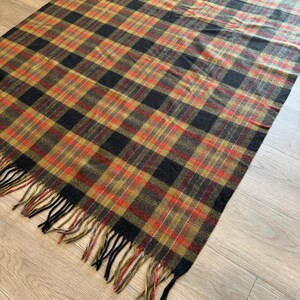 May include: A rectangular plaid blanket in shades of black, brown, red, and gold. The blanket has a fringed edge. The plaid pattern is a classic design, suitable for a variety of uses.