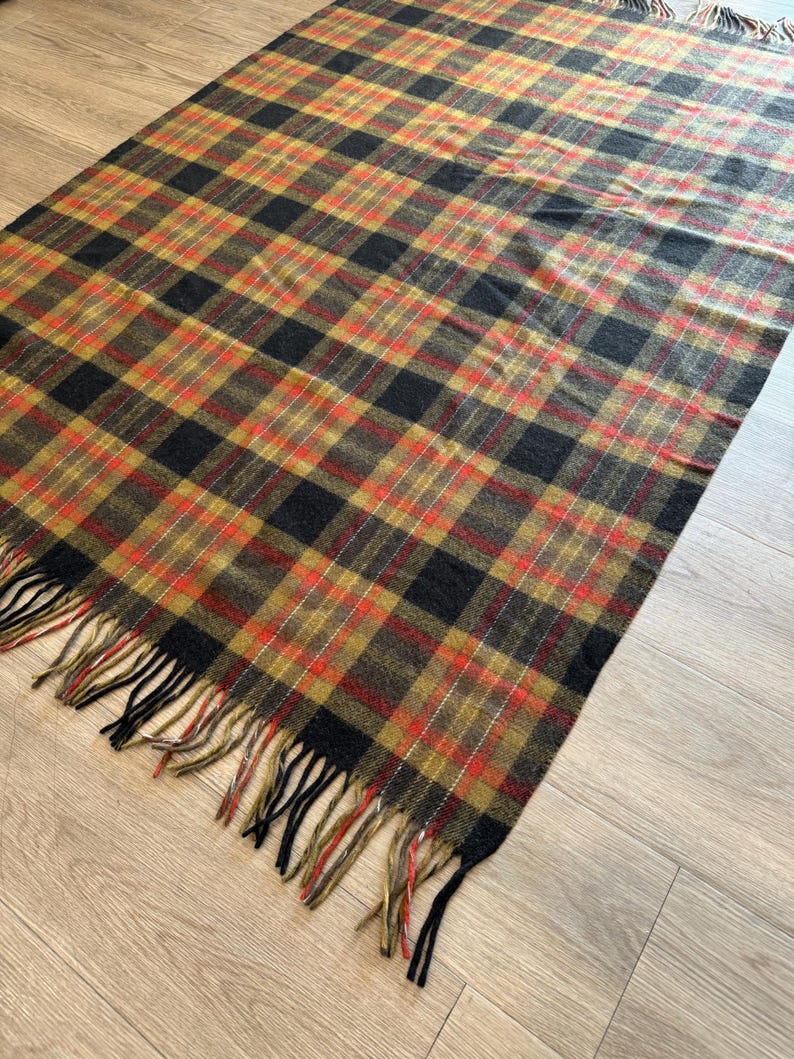 May include: A rectangular plaid blanket in shades of black, brown, red, and gold. The blanket has a fringed edge. The plaid pattern is a classic design, suitable for a variety of uses.