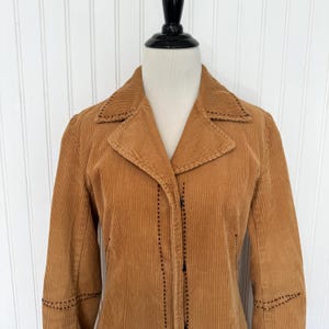 May include: A tan corduroy jacket with a notched collar and long sleeves. The jacket features decorative stitching along the collar, cuffs, and seams. It is buttoned up and displayed on a mannequin.