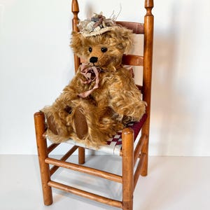 May include: A brown teddy bear wearing a white and brown hat sits on a wooden chair with a woven seat. The chair has a simple design with turned legs and a ladder back.
