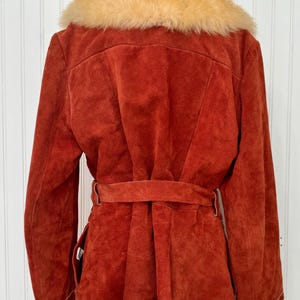 May include: A rust-colored suede jacket with a tan faux fur collar. The jacket features a belt at the waist and a tailored fit. The back view shows the details of the collar and the belt.