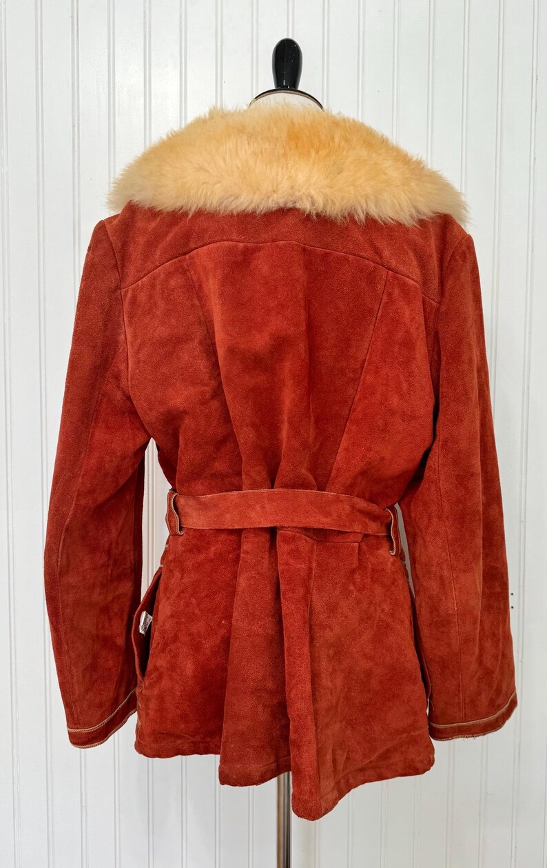 May include: A rust-colored suede jacket with a tan faux fur collar. The jacket features a belt at the waist and a tailored fit. The back view shows the details of the collar and the belt.