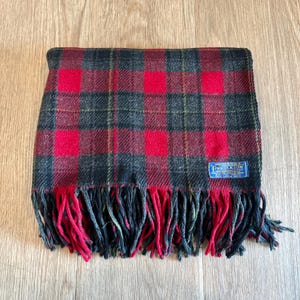 Puede incluir: Bufanda a cuadros rojos, negros y verdes con flecos. La bufanda tiene forma rectangular y una etiqueta que dice "Pendleton". La bufanda est&aacute; hecha de un material suave y es adecuada para el clima fr&iacute;o.