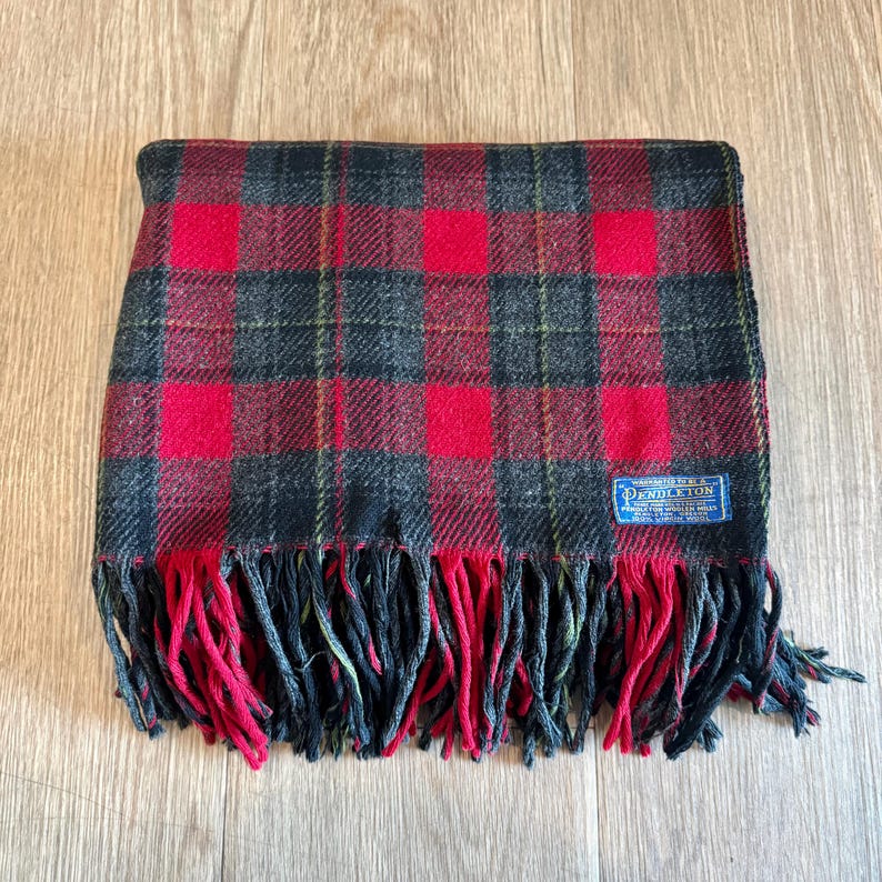 Puede incluir: Bufanda a cuadros rojos, negros y verdes con flecos. La bufanda tiene forma rectangular y una etiqueta que dice "Pendleton". La bufanda est&aacute; hecha de un material suave y es adecuada para el clima fr&iacute;o.