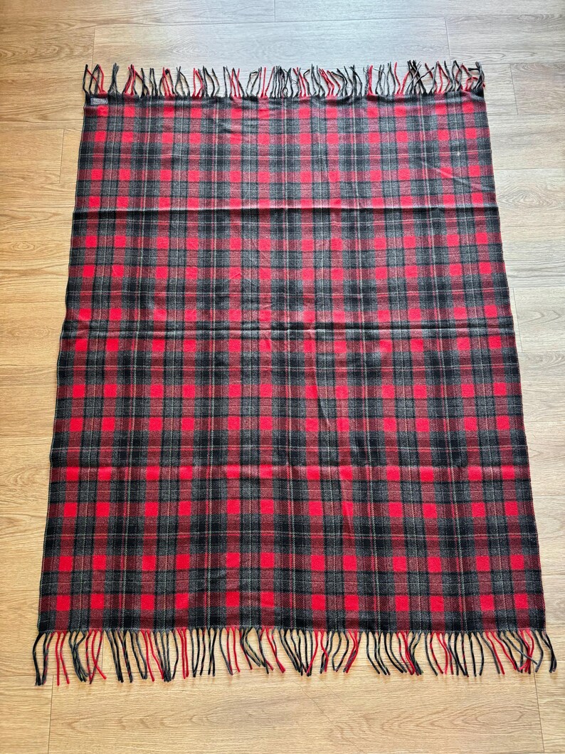 Puede incluir: Una manta rectangular a cuadros rojos, negros y grises, con flecos en los bordes superior e inferior. La manta presenta un patr&oacute;n de tart&aacute;n cl&aacute;sico, adecuado para la decoraci&oacute;n del hogar o para uso en exteriores.