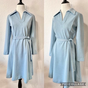 May include: A light blue vintage dress with a long sleeve, a collar, and a tie belt. The dress has a v-neckline and a slightly flared skirt.