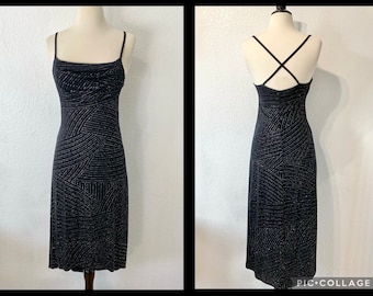 May include: A black midi dress with a silver glitter pattern. The dress has a cowl neck and spaghetti straps. The back of the dress has a criss-cross strap detail.