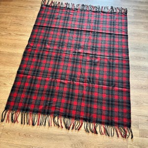 Puede incluir: Una manta rectangular a cuadros rojos y negros con borde de flecos. La manta presenta un dise&ntilde;o de tart&aacute;n cl&aacute;sico, con gruesas l&iacute;neas negras que se cruzan sobre un fondo rojo. El borde con flecos a&ntilde;ade un toque decorativo.