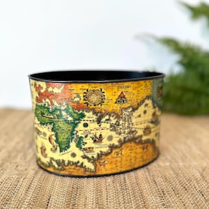 May include: A cylindrical metal planter with a black rim and a vintage world map design. The map features a yellow background with green, orange, and brown continents. The planter is suitable for indoor or outdoor use.