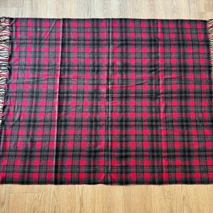 Puede incluir: Una manta rectangular a cuadros rojos y negros con bordes con flecos. La manta presenta un patr&oacute;n de tart&aacute;n cl&aacute;sico con una cuadr&iacute;cula repetida de cuadrados rojos y l&iacute;neas negras. Los bordes con flecos a&ntilde;aden un toque decorativo.