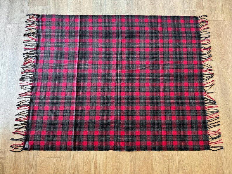 Puede incluir: Una manta rectangular a cuadros rojos y negros con bordes con flecos. La manta presenta un patr&oacute;n de tart&aacute;n cl&aacute;sico con una cuadr&iacute;cula repetida de cuadrados rojos y l&iacute;neas negras. Los bordes con flecos a&ntilde;aden un toque decorativo.