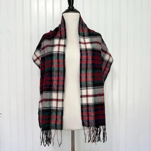 May include: A plaid scarf in red, green, black, and white, displayed on a mannequin. The scarf has a fringed edge and a classic tartan pattern. The scarf is made of a soft, woven material, perfect for adding warmth and style.
