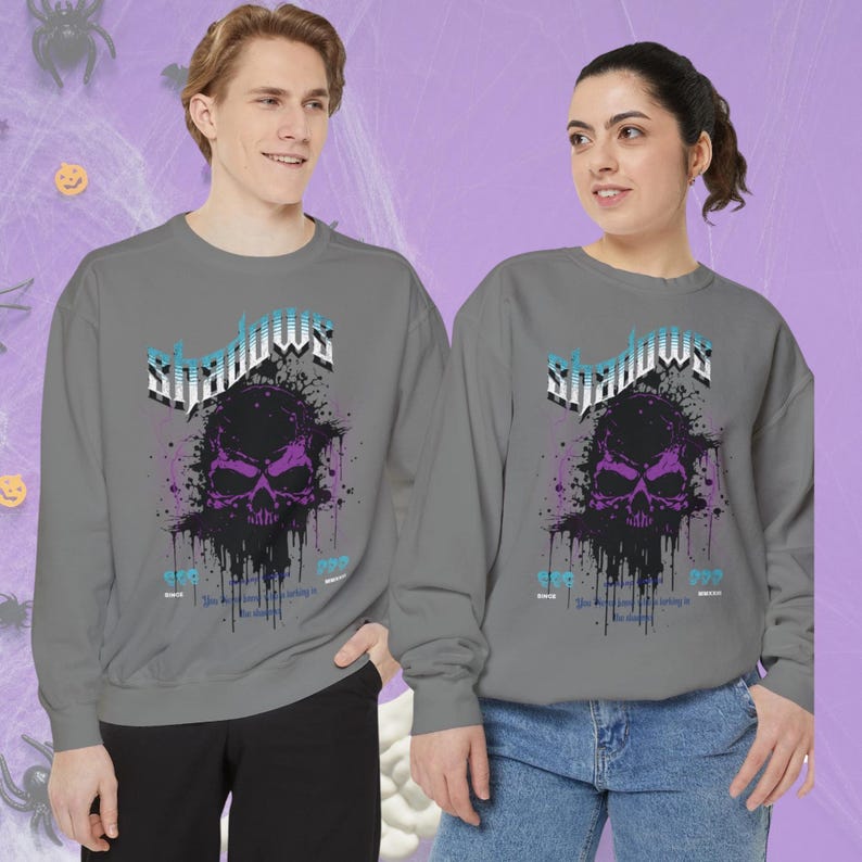 A man and a woman wearing matching gray crewneck sweatshirts with a purple and black skull design, splattered with black ink, and the word "Shadows" above it in blue and white.