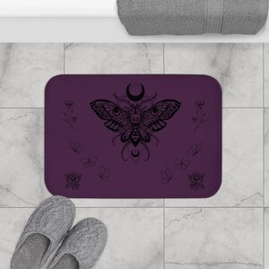 a purple beach towel with a design of the moon and butterfly, surrounded by various beach-related items such as a smartphone, flip flops, and seashells.