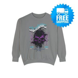 A gray crewneck sweatshirt with a purple and black skull design, splattered with black ink, and the word "Shadows" above it in blue and white.