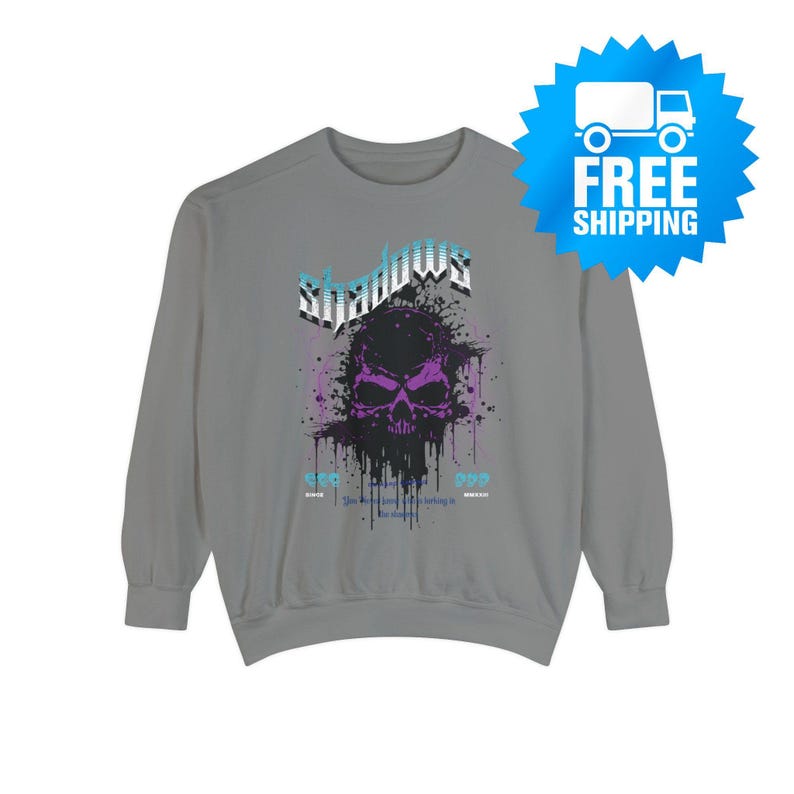 A gray crewneck sweatshirt with a purple and black skull design, splattered with black ink, and the word "Shadows" above it in blue and white.