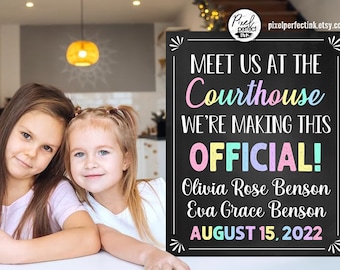May include: A chalkboard sign with the text "Meet us at the Courthouse We're making this Official! Olivia Rose Benson Eva Grace Benson August 15, 2022". The sign is decorated with colorful chalk drawings and a pink, blue, yellow, and green color scheme.