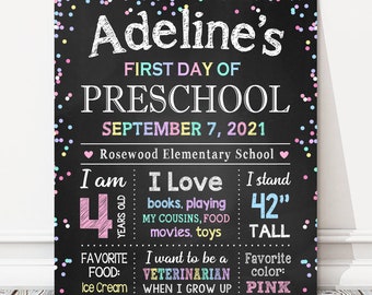 May include: A black chalkboard sign with colorful confetti and the text "Adeline's First Day of Preschool September 7, 2021 Rosewood Elementary School". The sign also includes information about Adeline, such as her age, favorite things, and future aspirations.