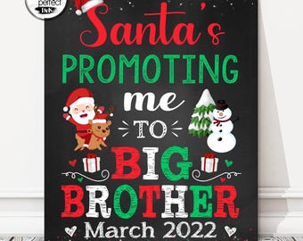 May include: A black sign with the text "Santa's Promoting me TO BIG BROTHER March 2022". The sign features illustrations of Santa Claus, a reindeer, a snowman, and a Christmas tree. The text is in red, green, and white.