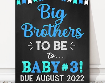 May include: A chalkboard-style sign with the text "Big Brothers TO BE to... BABY #3! DUE AUGUST 2022". The text is in blue and white, with decorative bunting across the top.