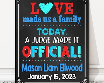 May include: A chalkboard sign with the text "LOVE made us a family TODAY, A JUDGE MADE IT OFFICIAL! Mason Liam Ellwood January 15, 2023". The text is in red, blue, and white, and the background is black.