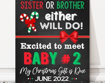 May include: A black sign with red and green text that reads "SISTER OR BROTHER either WILL DO!" and "Excited to meet BABY #2." The sign also says "My Christmas Gift is Due JUNE 2022."