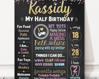 May include: A chalkboard sign with a pink, gold, and blue confetti background. The sign says "Kassidy My Half Birthday" and includes details about the child's age, weight, height, favorite foods, toys, and songs.