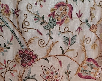 May include: Close-up of embroidered fabric with a floral design. The embroidery features a cream-colored background with brown, green, pink, and yellow floral patterns. The design includes flowers, leaves, and vines, creating a detailed and textured appearance.
