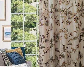 May include: Beige sheer curtains with an embroidered floral pattern in shades of green, brown, and purple. The curtains are hung in a living room setting.