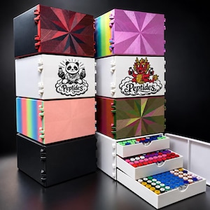 Op de afbeelding: Een stapel rechthoekige opbergdozen met diverse afwerkingen, waaronder effen zwart, regenboogverlopen en geometrische patronen. Twee witte dozen bevatten grafische illustraties van een panda en een draak met de tekst Peptides. Drie open lades bevatten rijen kleine kleurrijke flesjes.