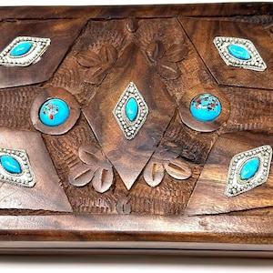 May include: A wooden box with a carved design and inlaid turquoise stones. The box has a hinged lid and is made of dark wood.