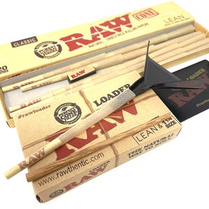 May include: A collection of RAW brand rolling papers, cones, and a loader. The packaging is tan and red, with text including "RAW," "Classic," and "Lean." The image shows a box of cones, a loader tool, and a pre-rolled cone.