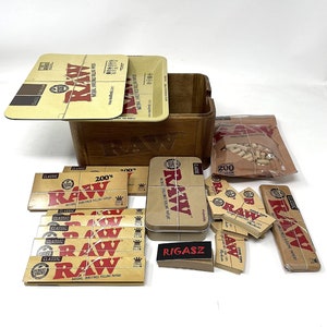 May include: A wooden box with a RAW logo on the front, filled with various RAW rolling papers, cone tips, and a tin of RAW rolling papers. The box also includes a pack of 200 cellulose filters.