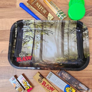 Può includere: Un vassoio in metallo per arrotolare con un design a tema foresta. Il vassoio è circondato da vari tipi di cartine per sigarette, tra cui RAW, Zapa, Juicy Jay's, The Bulldog e Rizla. Ci sono anche un macinino verde e un cono per arrotolare blu.