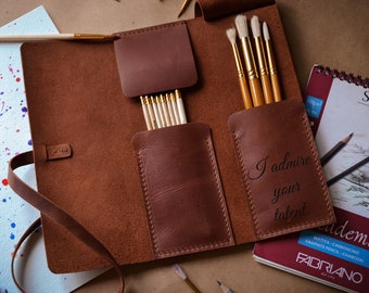 May include: A brown leather roll-up case for holding art supplies. The case has a strap and is open to reveal multiple slots for brushes and pencils. The case is personalized with the text "I admire your talent".
