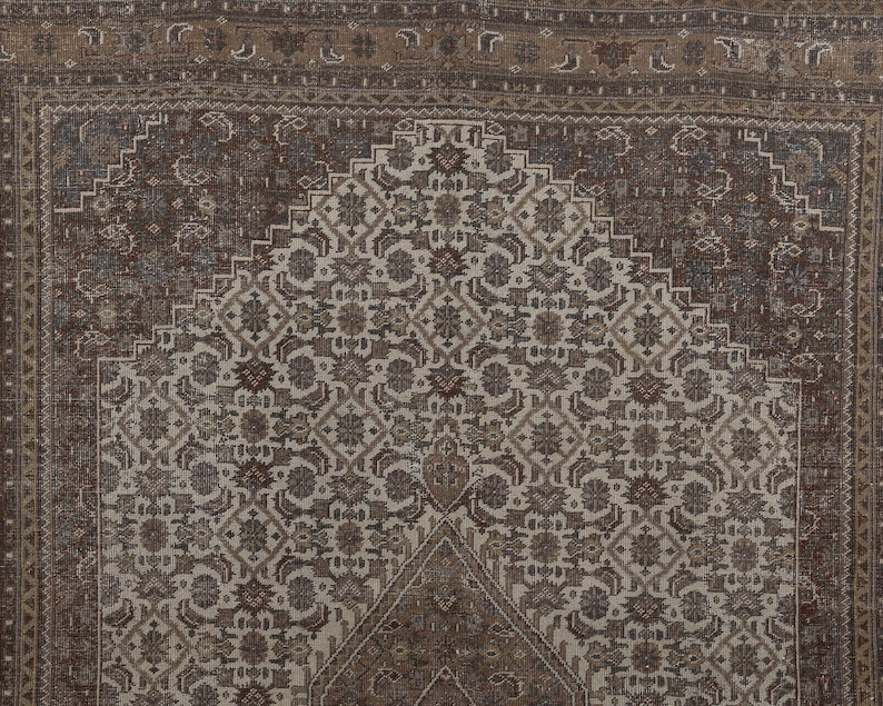 May include: A detailed, close-up view of a vintage rug. The rug features a central design in cream and brown tones, with intricate floral and geometric patterns. The border is a darker brown, framing the central design. The rug's texture and design suggest it is a traditional, handmade piece.