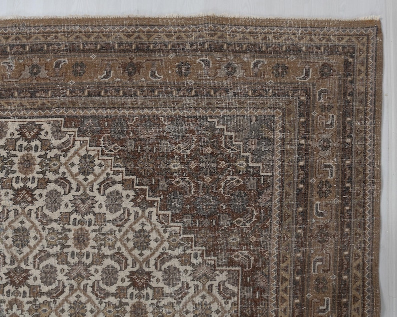 May include: Close-up of a section of a vintage rug with a detailed, ornate design. The rug features a central pattern in cream and brown tones, surrounded by a border in shades of brown and tan. The intricate patterns and color palette suggest a traditional style.
