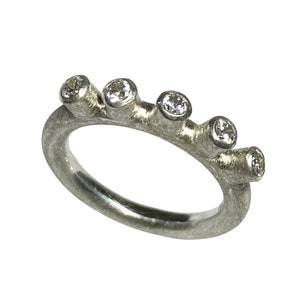 Könnte beinhalten: Ein silberner Ring mit fünf kleinen Diamanten, die in die Band gefasst sind. Die Band ist texturiert und hat ein raues, organisches Aussehen.
