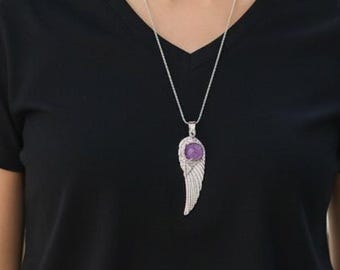 May include: A black V-neck t-shirt paired with dark denim jeans and a silver-toned necklace featuring a pendant shaped like an angel wing with a round, purple gemstone set at the top of the wing structure.
