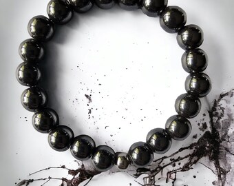 Op de afbeelding: Een zwarte kralen armband met een zilveren accent. De armband is gemaakt van ronde, gladde kralen en ligt op een wit oppervlak.