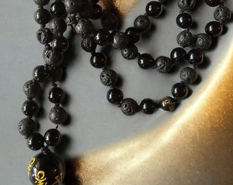 Op de afbeelding: Zwarte lavastenen mala-ketting met een zwarte obsidiaan Boeddha-hanger. De ketting is gemaakt van 108 kralen en is ongeveer 46 cm lang.