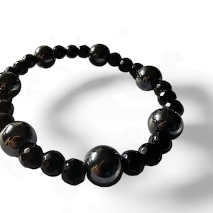 Op de afbeelding: Een zwarte kralen armband met afwisselend grote en kleine kralen. De grote kralen zijn rond en glad, terwijl de kleine kralen gefacetteerd zijn.