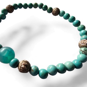 May include: Turquoise and silver beaded bracelet with a larger turquoise bead. The bracelet is made of small round beads with a silver accent on each bead.