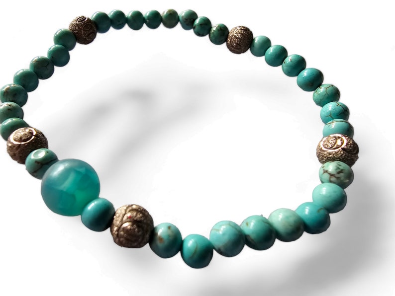 May include: Turquoise and silver beaded bracelet with a larger turquoise bead. The bracelet is made of small round beads with a silver accent on each bead.