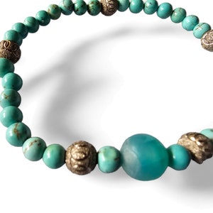 May include: Turquoise blue beaded bracelet with silver accents. The bracelet features a large turquoise blue bead in the center.